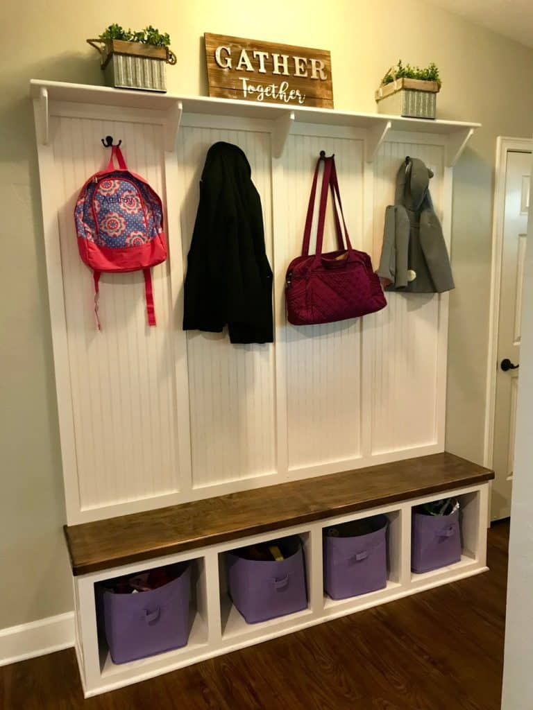 An example of a mudroom. Pictures shows a bench with coats and backpacks hanging from hooks. 