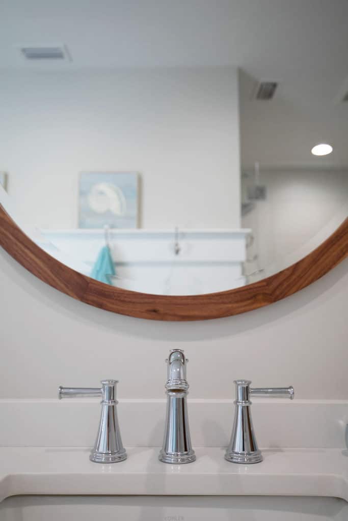 A wooden, round wall mirror above a bathroom vanity.