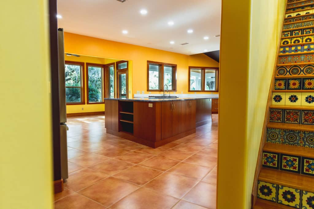 Interior Home Renovation - View of kitchen with tile flooring and granite island. View of decorative staircase on the right side of the image.