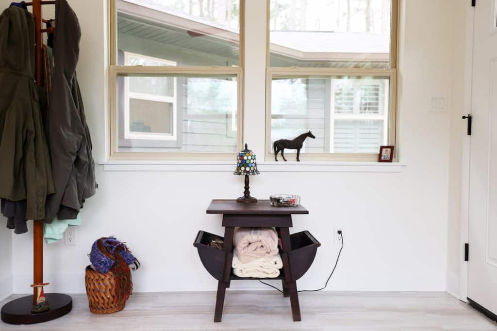 Interior or a well-lit entryway with double windows next to a white door aside table and coatrack 