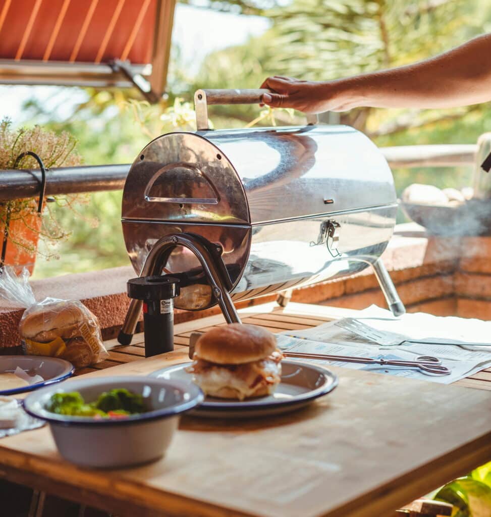 Simple table top patio grill in a compact outdoor kitchen alongside freshly prepared burgers and grilled vegetables. 