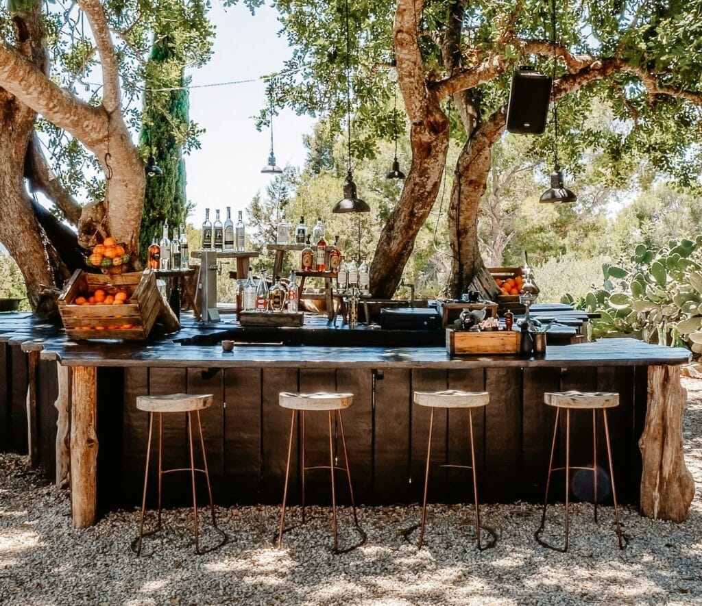 Topical outdoor kitchen with bar area and stools among trrees 